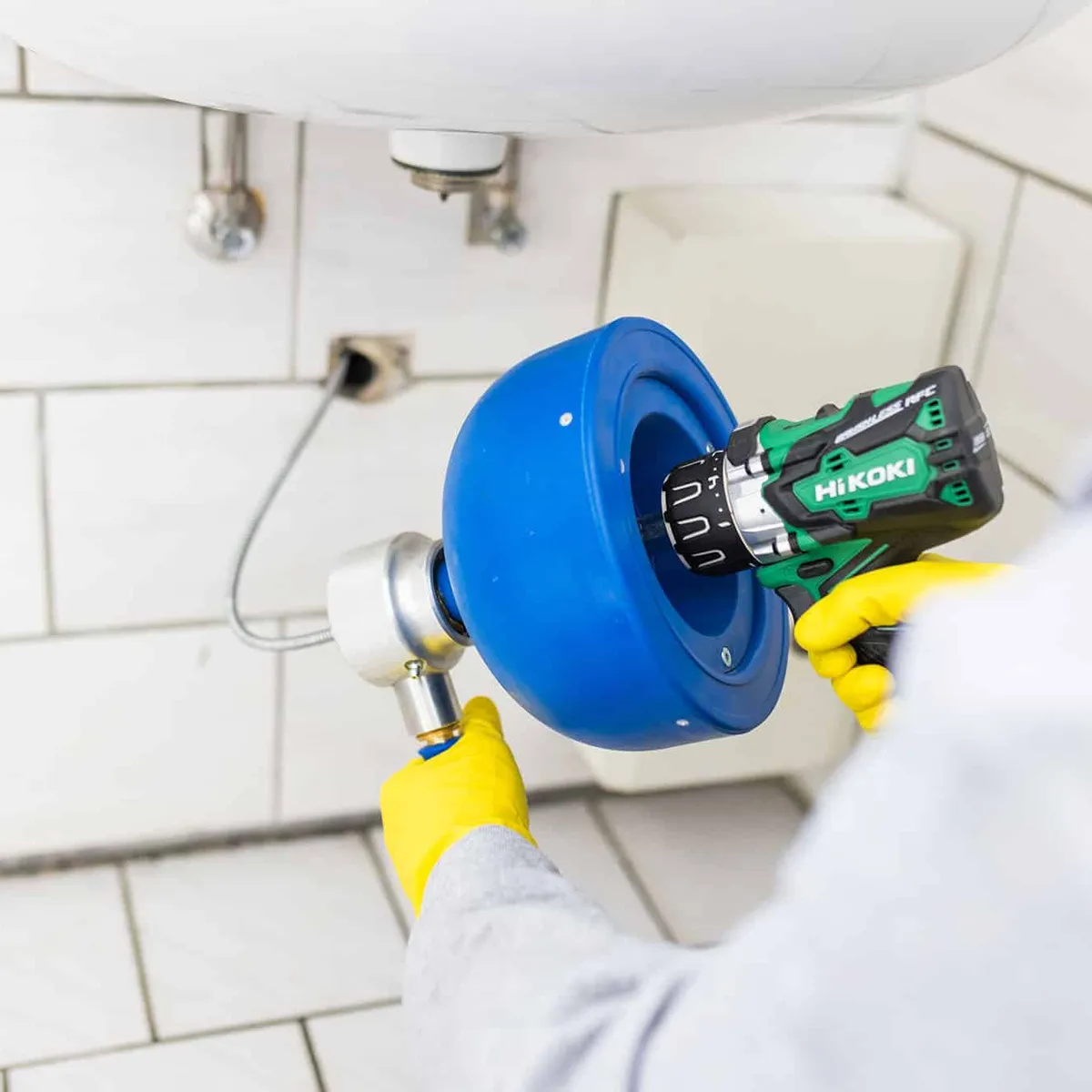 Techniker setzt eine Rohrreinigungsmaschine am Waschbeckenabfluss an