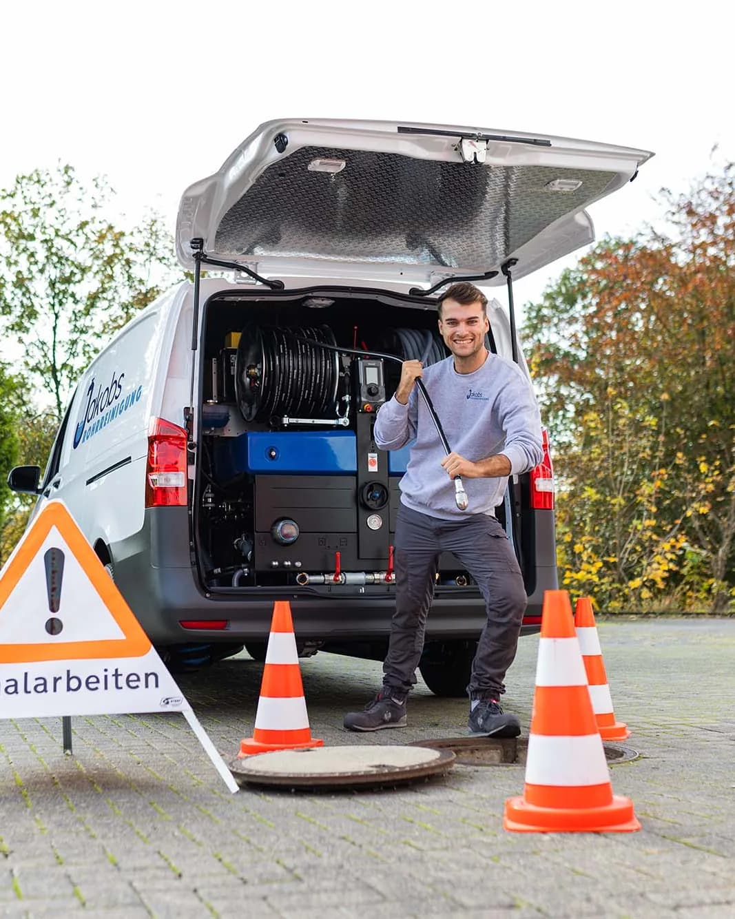 Techniker der Jakobs Rohrreinigung mit Reinigungsspirale am abgesicherten Kanalschacht